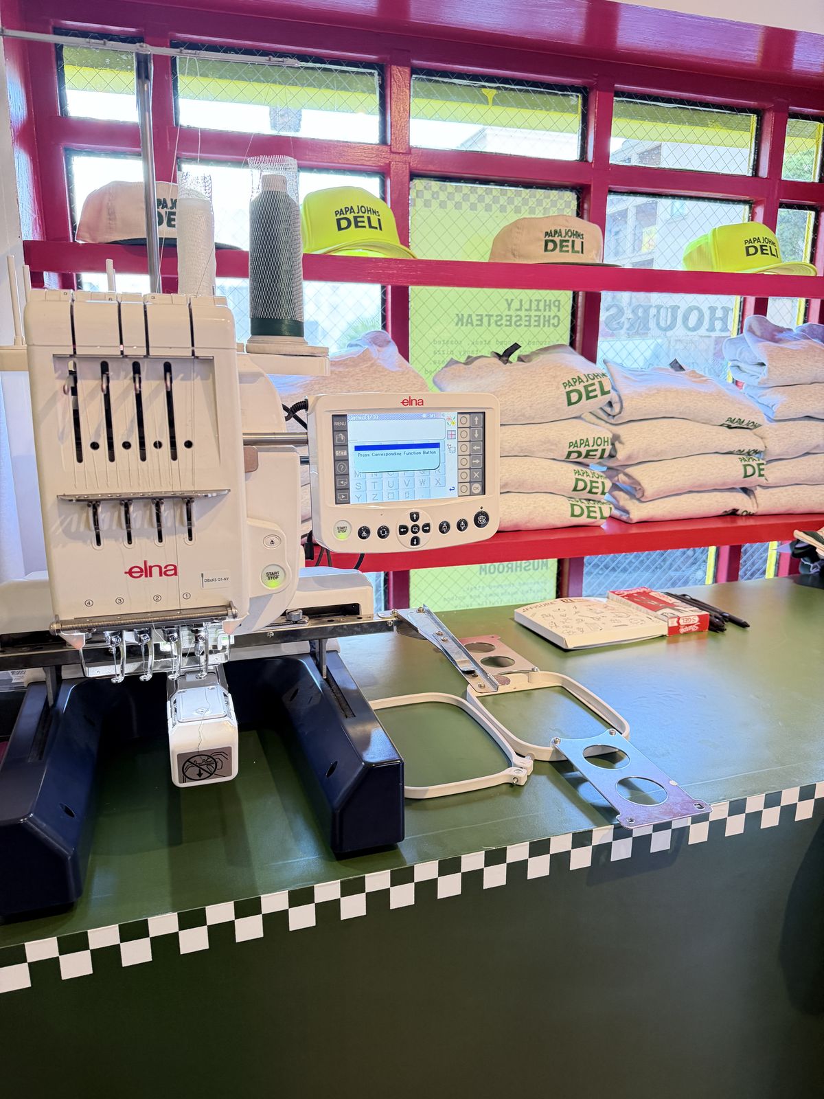 Embroidery machine set up beside a shelf of blank trucker hats at a hat bar station